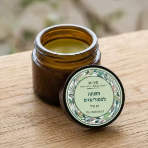משחה טבעית לפסוריאזיס בצנצנת זכוכית עם מכסה, לצד עלי צמחי מרפא ברקע